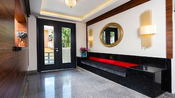 Un vestíbulo moderno con un mostrador de recepción negro, un banco rojo, un espejo redondo y una lámpara fijada a la pared.