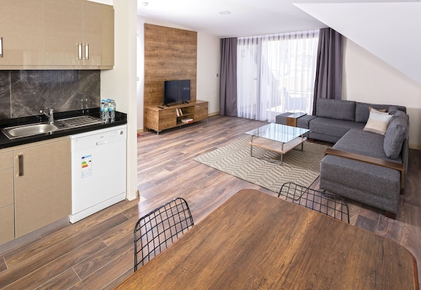 A modern apartment with a kitchen, dining area, and living room. It features a wooden floor, a sofa, a coffee table, and a TV.