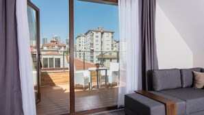 A modern living room with a grey sofa, a wooden coffee table, and a sliding glass door leading to an outdoor patio with a table and chairs. - Princess Residence (Istanbul)