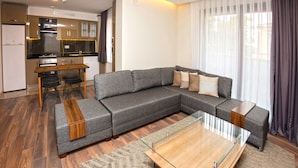 A modern living room with a sectional sofa, a glass coffee table, and a kitchen in the background. - Princess Residence (Istanbul)
