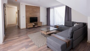 A modern living room with a grey sofa, a glass coffee table, a wooden entertainment unit, and a herringbone-patterned rug. - Princess Residence (Istanbul)
