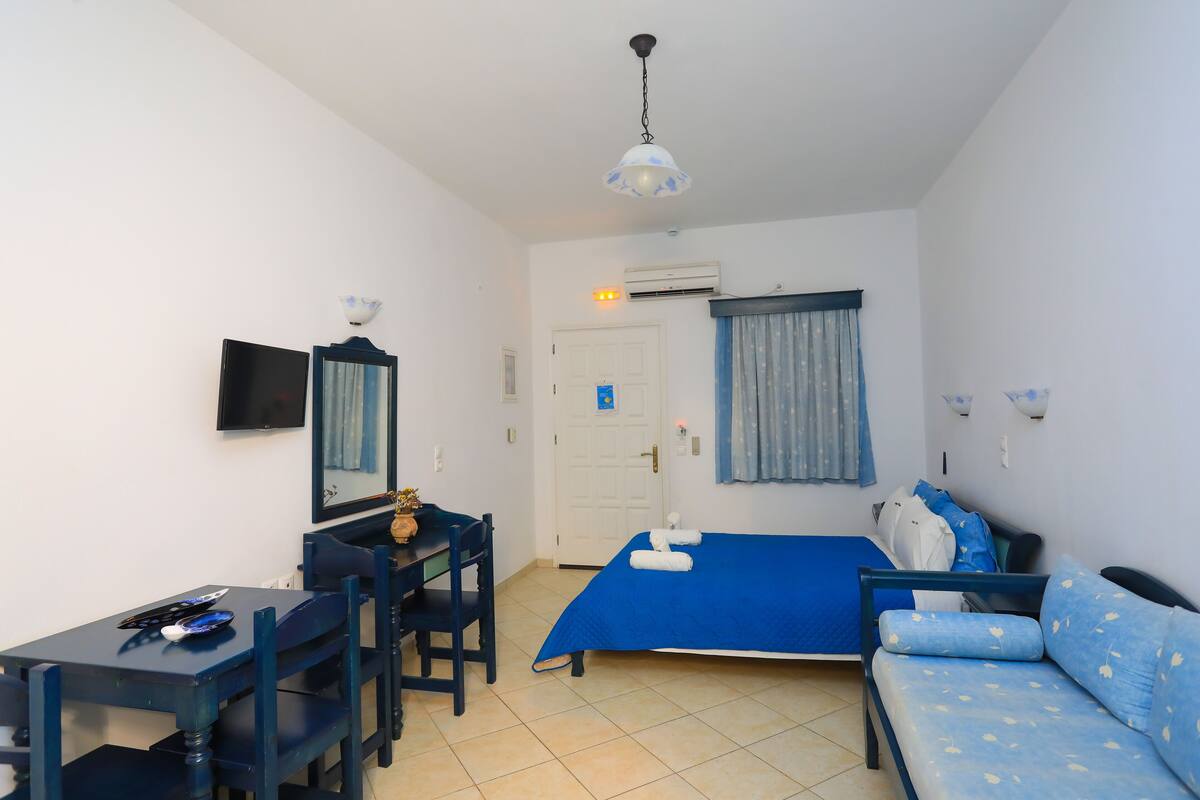 Een kleine, schone kamer met een bed, een bureau, een stoel, een bank en een televisie.
