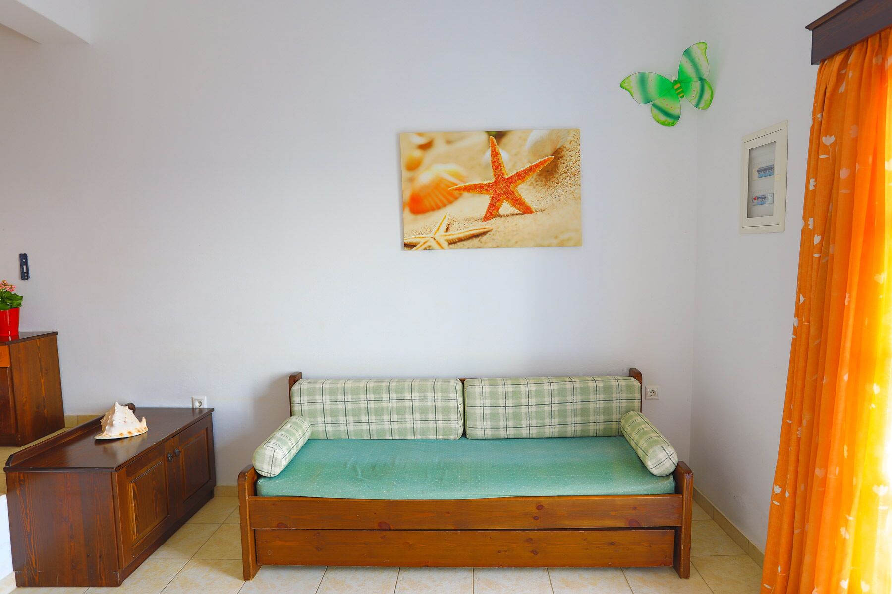 A room with a wooden bench, a wall-mounted picture of a starfish, and a green butterfly decoration.