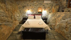Een kamer met stenen muren, een bed, twee nachtkastjes en een bank.