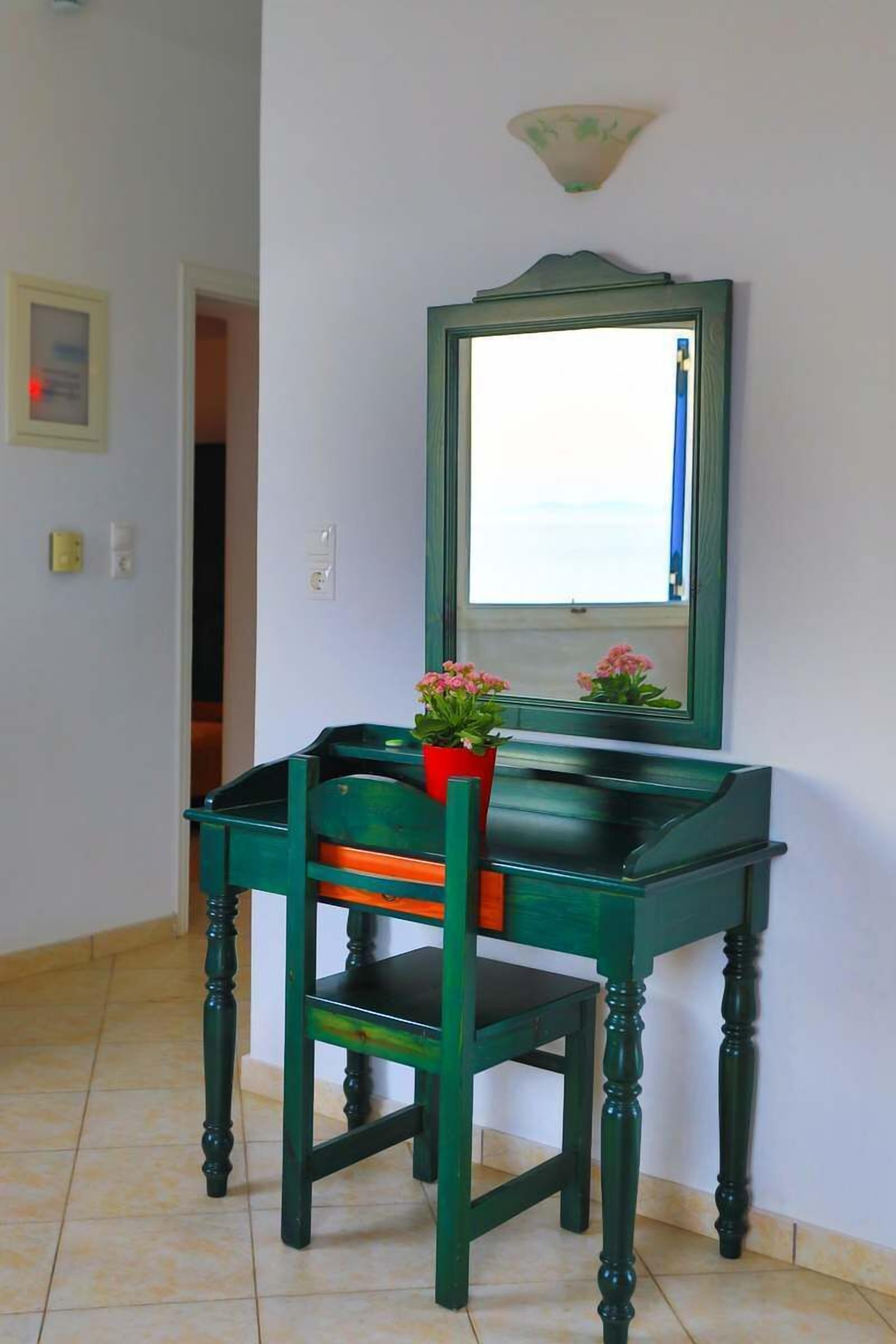 Un escritorio verde con una silla, un espejo y una planta en maceta.