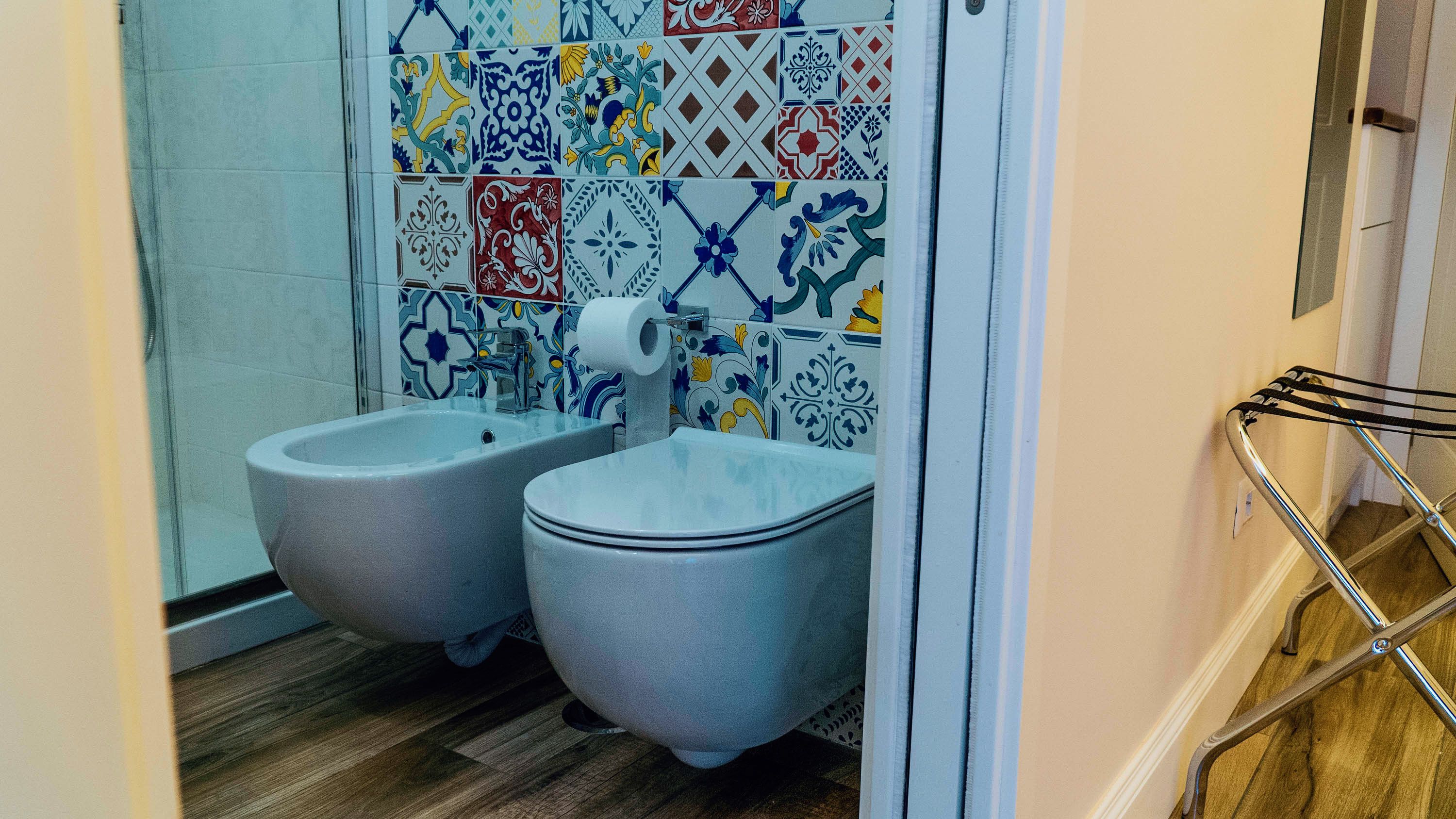 A bathroom with two bidets, a shower, and a tiled wall with a variety of patterns.