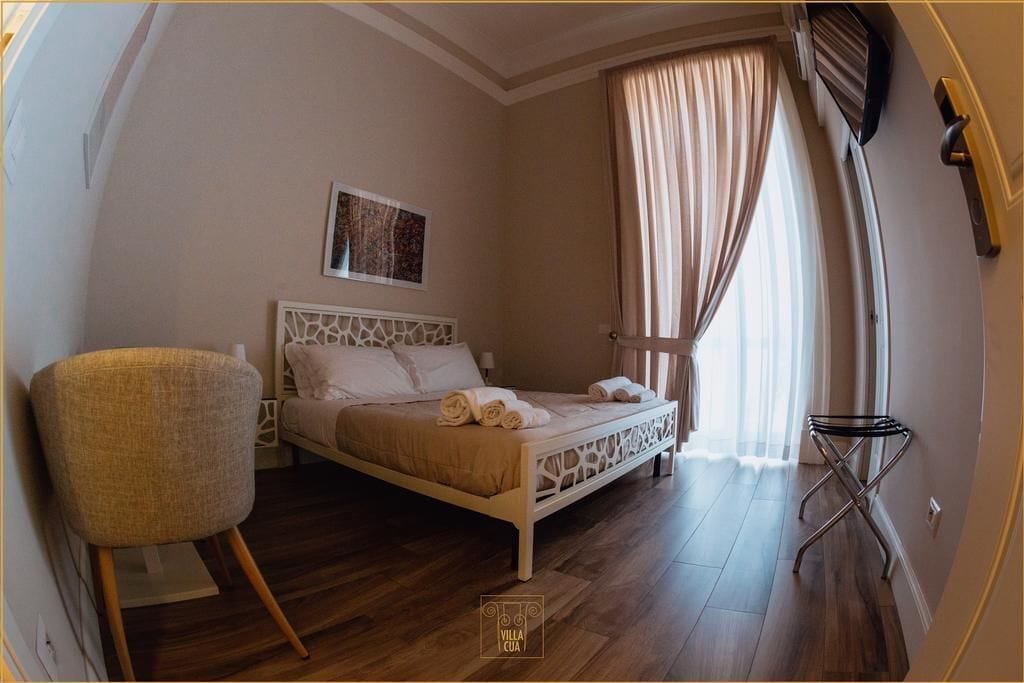 A bedroom with a bed, a chair, a window with curtains, and a door.