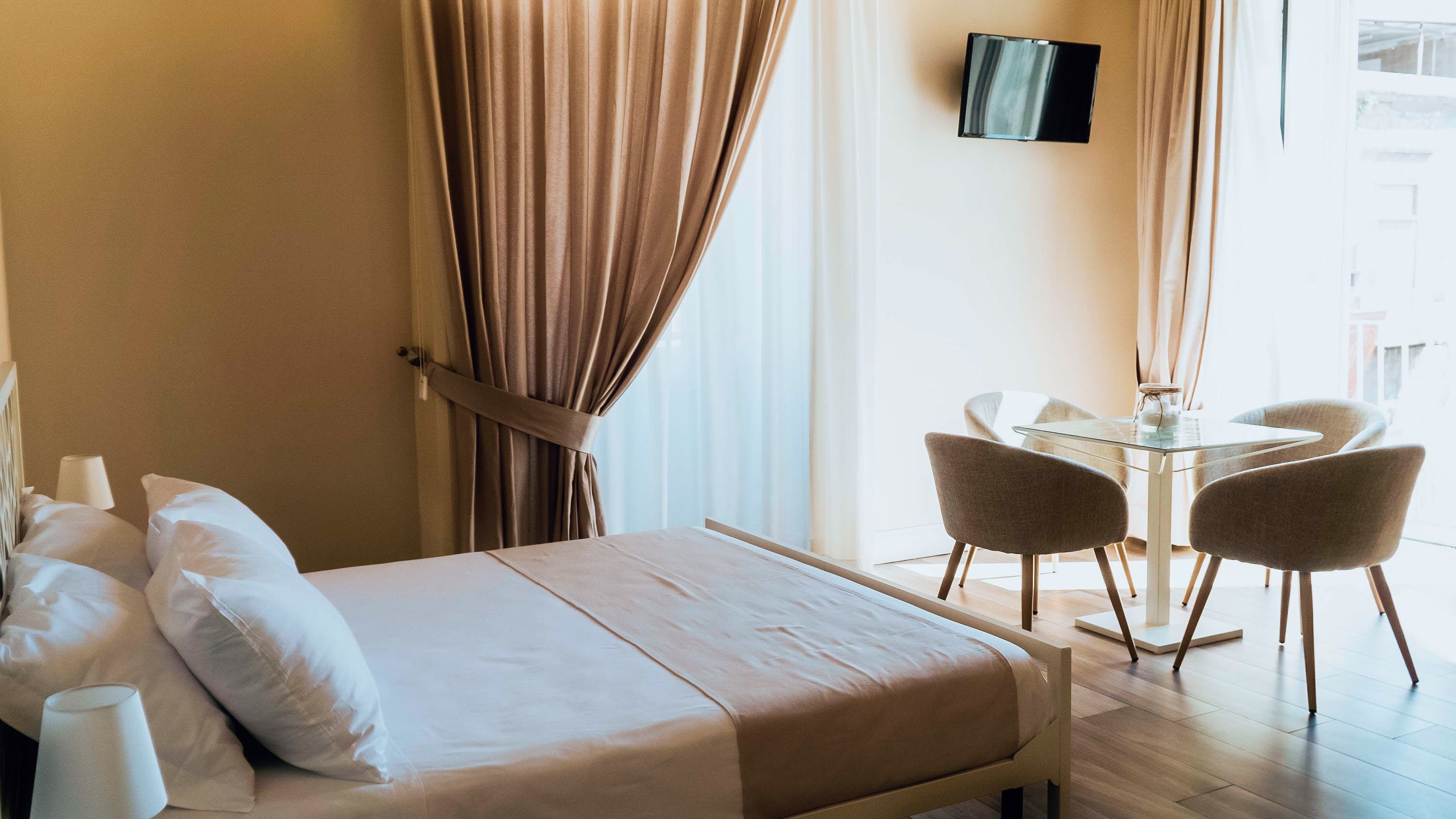 A hotel room with a bed, a desk, two chairs, and a TV on the wall.