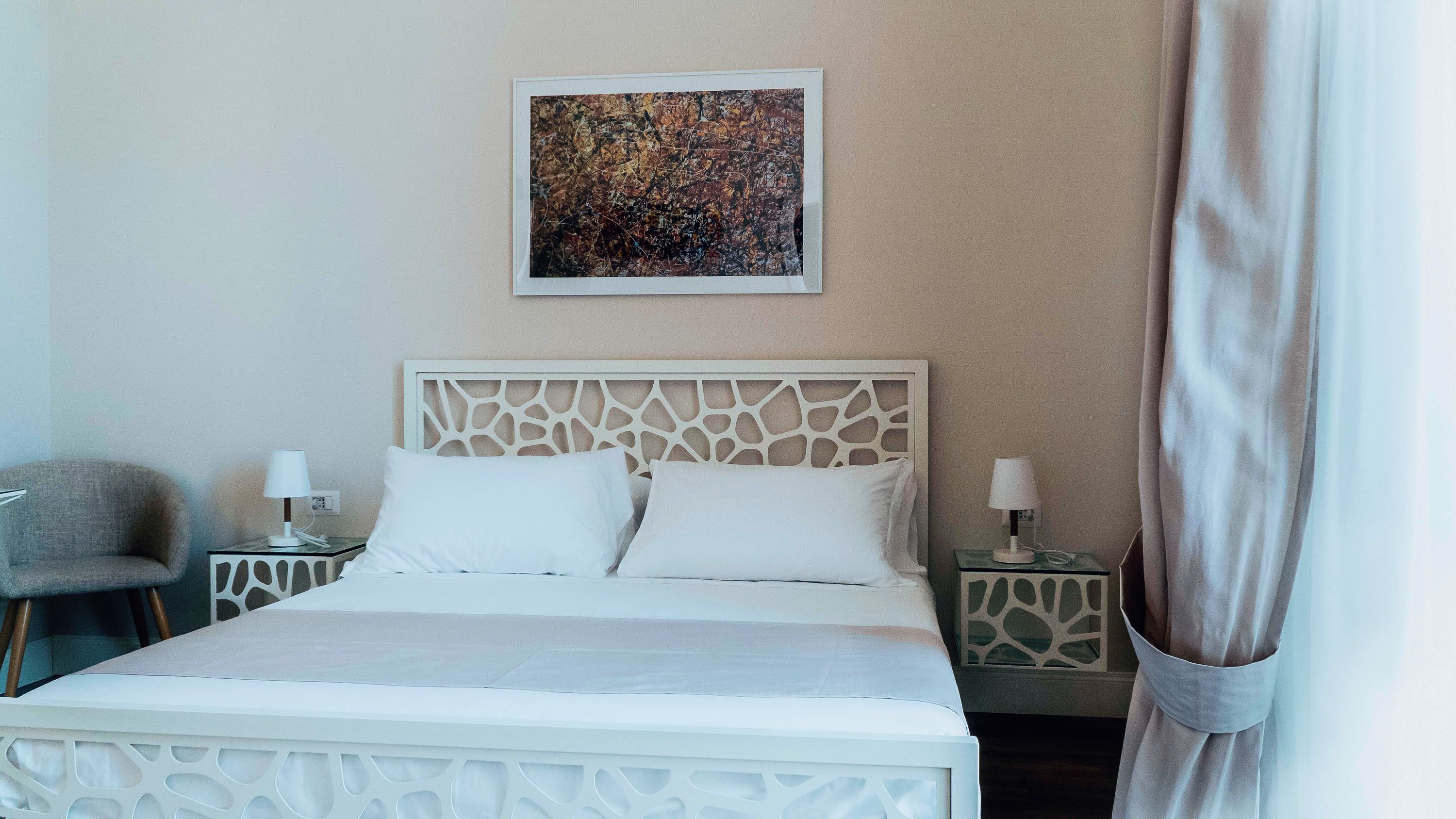 A hotel room with a bed, two bedside tables, a chair, and a painting on the wall.