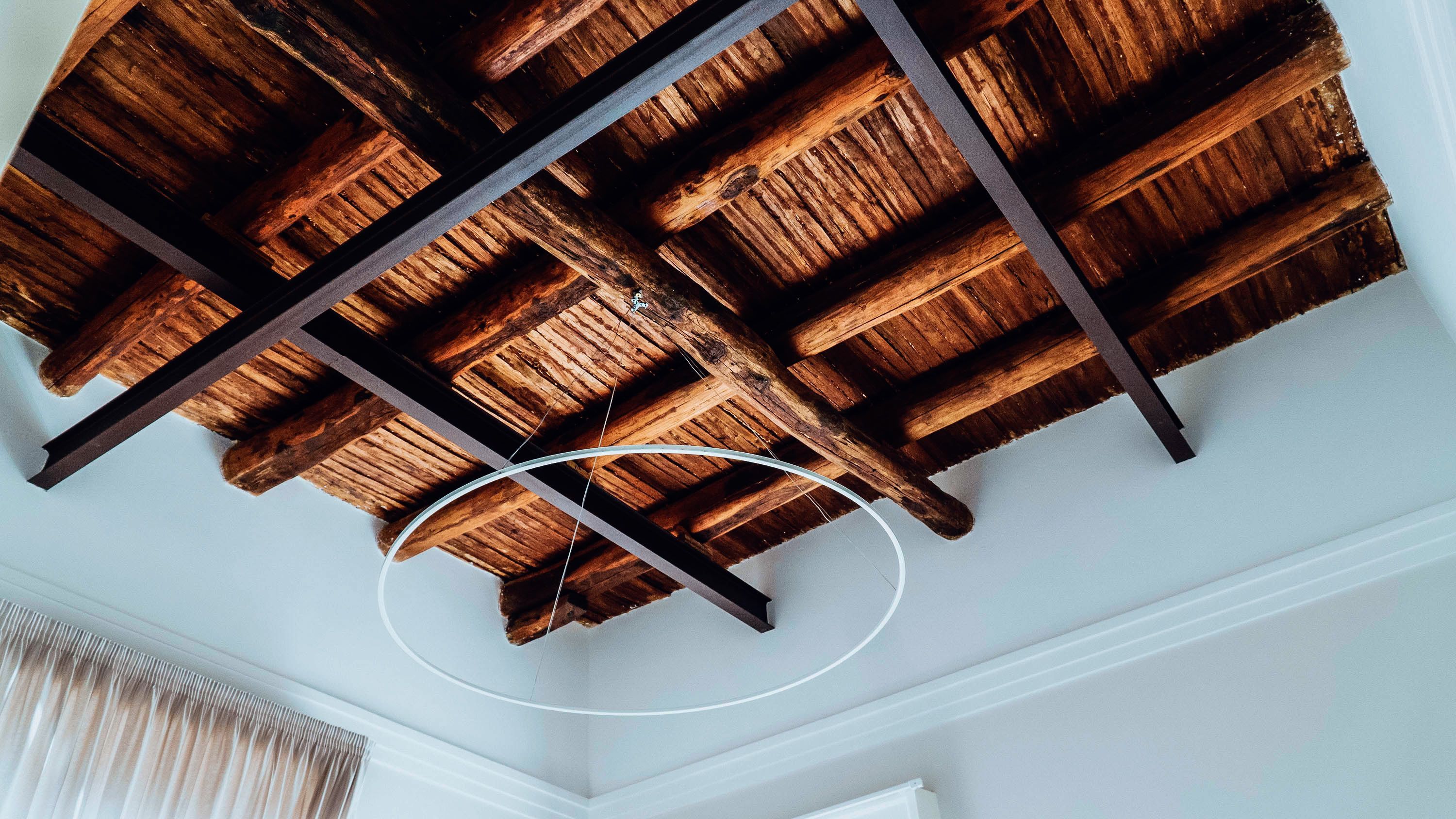 Una habitación con estructura de techo de madera, paredes blancas y una lámpara circular blanca.