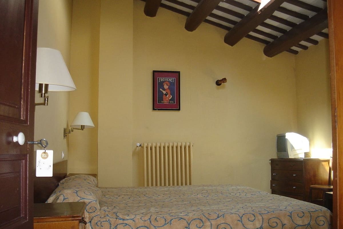 Un dormitorio con una cama, un radiador, un televisor sobre una cómoda y un cartel enmarcado en la pared.