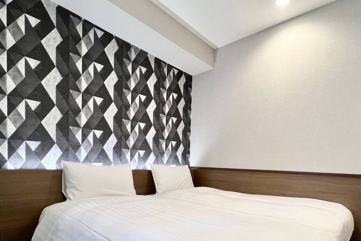 Una habitación de hotel con una cama grande, un cabecero de diseño geométrico y una pared lisa.