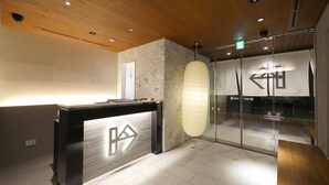 Un área de recepción con diseño moderno, que incluye un mostrador de recepción, un gran farol de papel y una puerta de cristal con un letrero.