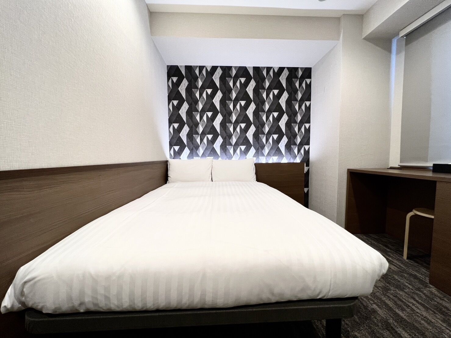 A hotel room with a bed, a desk, and a patterned headboard.