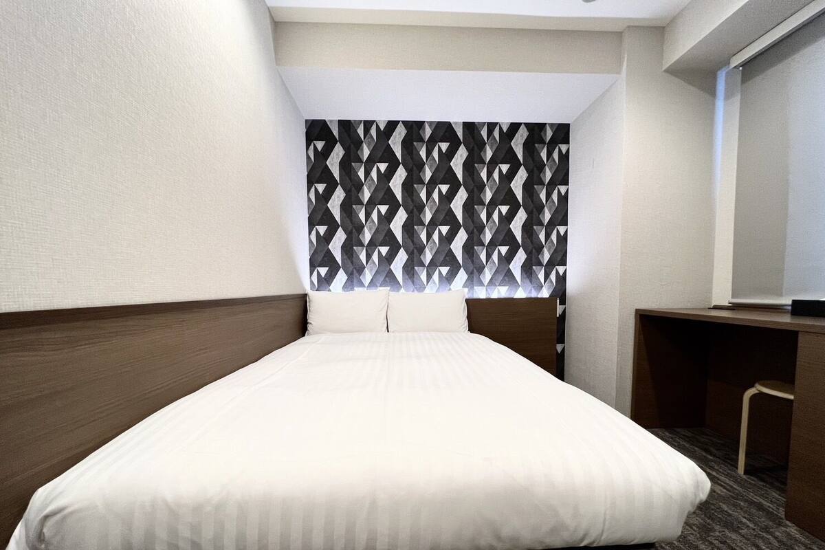 Habitación de hotel con cama, escritorio y cabecera estampada.
