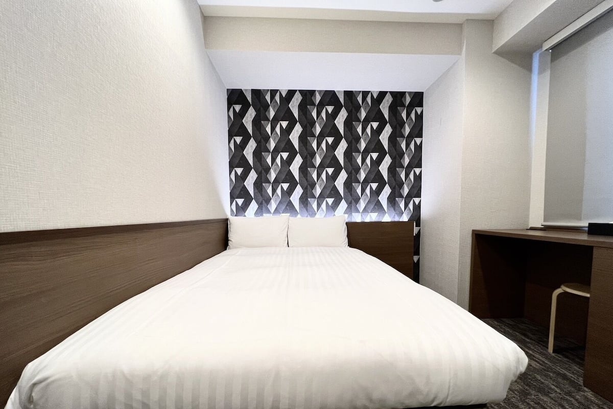 A hotel room with a bed, a desk, and a patterned headboard.