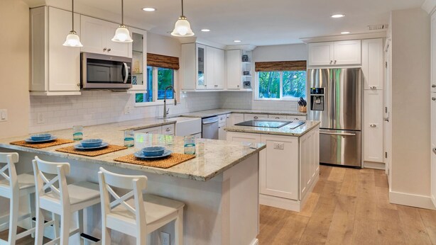 Cocina moderna con armarios blancos, una isla central con taburetes y un refrigerador de acero inoxidable, además de iluminación colgante.