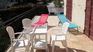 Un patio con sedie in plastica bianca e un tavolo, una poltrona rossa e una blu, e una vista sulle montagne sullo sfondo.