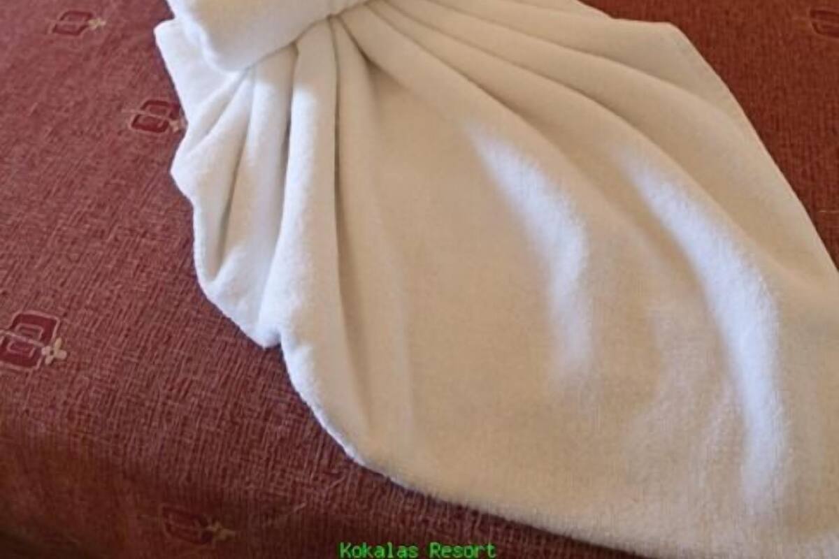 A hotel room with a bed covered in a red bedspread and a white towel folded on the bed.