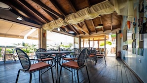 An outdoor dining area with wooden tables and chairs, a covered patio, and a view of the surrounding landscape. - Kokalas Resort (Apokoronas)