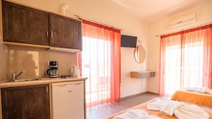 A hotel room with a kitchenette, a bed with towels, and a TV mounted on the wall. - Kokalas Resort (Apokoronas)