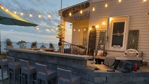 Un bar al mar amb un mostrador de pedra, cadires de vimet i llums penjants.
