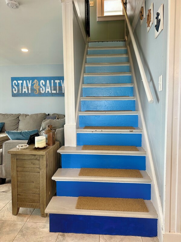 A staircase with blue steps and white railings, a wooden side table with a candle and a lantern, and a wall with a 'STAY SALT' sign. - Beach front property steps from Long Island Sound! (Westbrook)