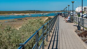 A wooden boardwalk with railings, leading to a beach with boats and a clear blue sky. - Exclusive T2 apartment in the center of Cabanas de Tavira (Cabanas de Tavira)