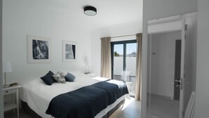 A modern bedroom with a large bed, a bedside table, a lamp, and two framed pictures on the wall. - Exclusive T2 apartment in the center of Cabanas de Tavira (Cabanas de Tavira)