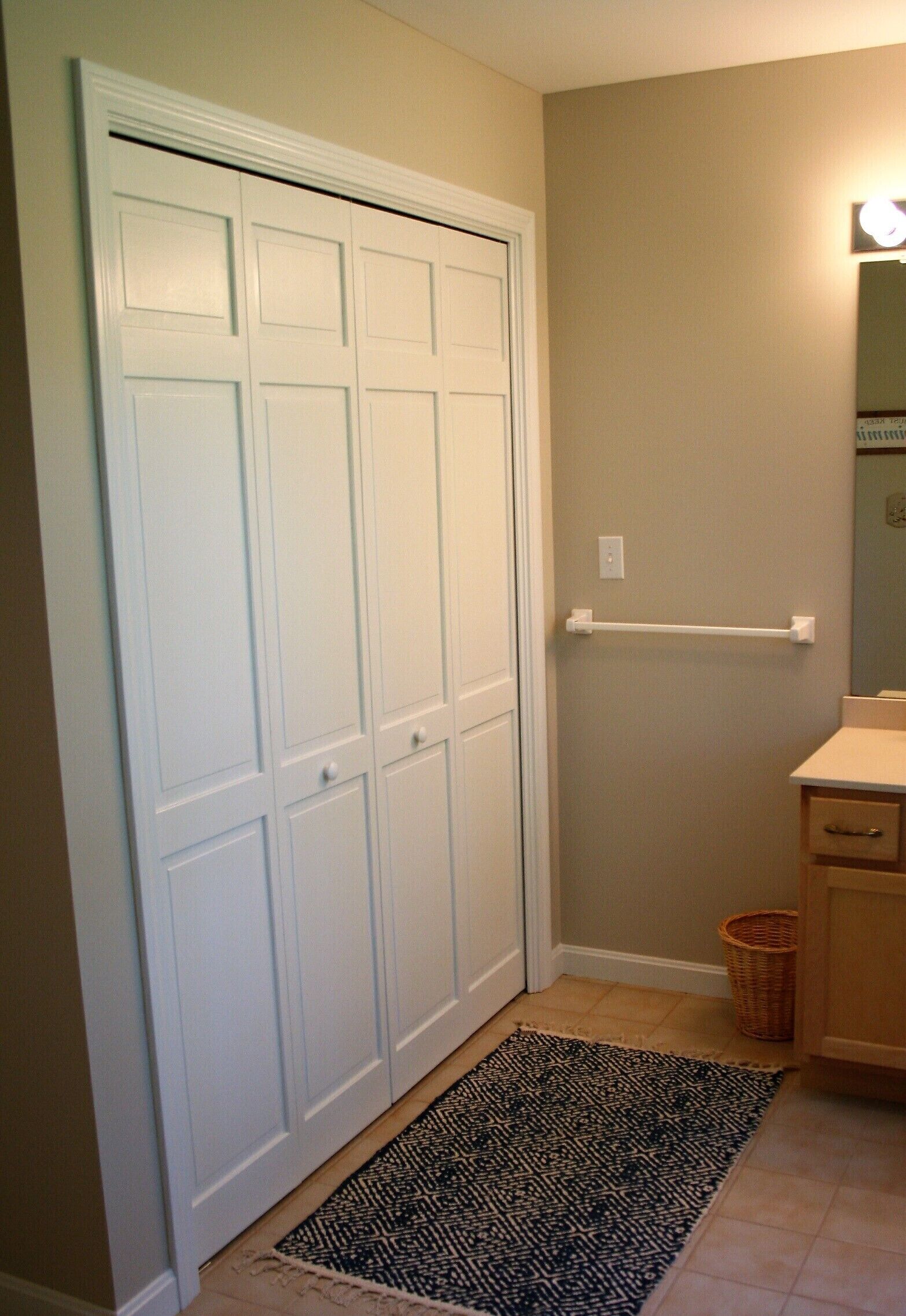 A hallway with a white closet, a black and white rug, a wooden basket, and a small mirror on the wall.