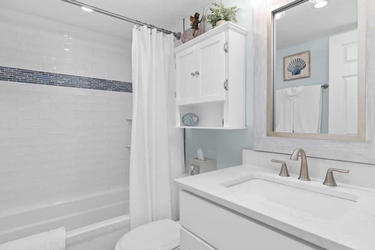 A bathroom with a white sink, a mirror, a toilet, and a shower curtain.