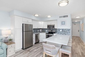 A modern kitchen with white cabinetry, stainless steel appliances, a large island, and a tiled backsplash. - Stunning Harborview Residence on Captiva Island (Captiva)