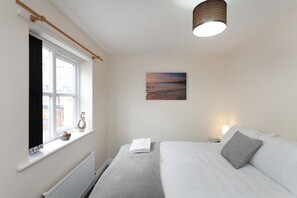 Ett sovrum med en säng, ett fönster med gardiner, en tavla på väggen och en taklampa.
