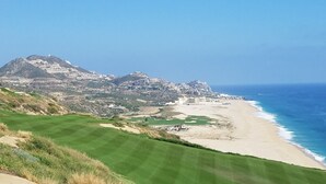 Eine Küstenansicht mit einem Golfplatz, Strand und Gebäuden an einem Hügelhang.