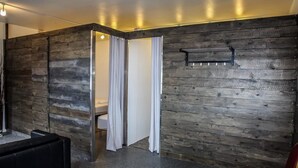 A modern room with a wooden wall, a black sofa, a red chair, and a white curtain. - Lava Apartment (Vestmannaeyjar)