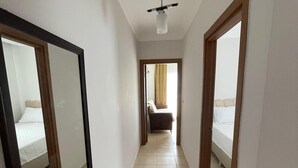 Un couloir étroit au sol carrelé, avec un ventilateur de plafond, et deux chambres dotées de lits et de rideaux.