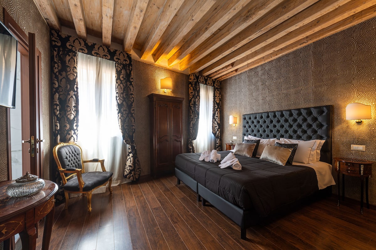 A bedroom with a large bed, a wooden ceiling, and a chair by the window.