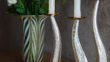 Tres velas blancas sobre soportes de plata, con un jarrón de flores blancas al fondo.