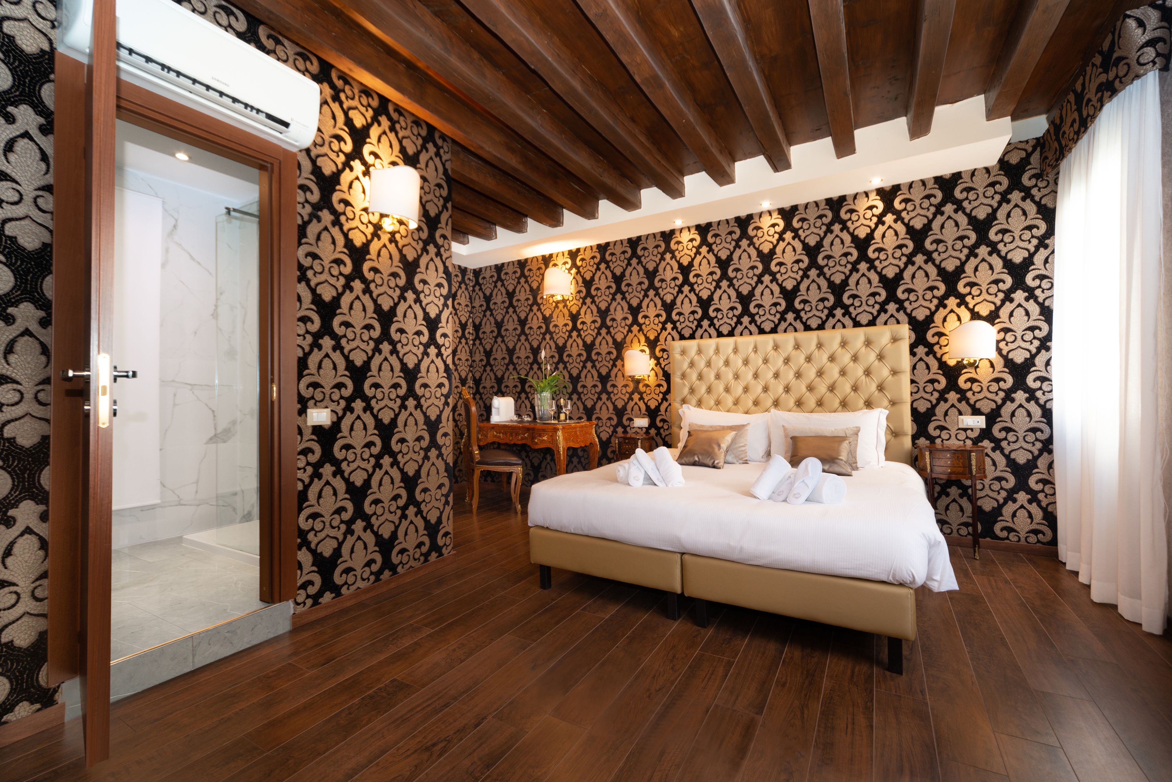 Un dormitorio con una cama grande, vigas de madera en el techo, papel tapiz estampado y dos lámparas de noche.