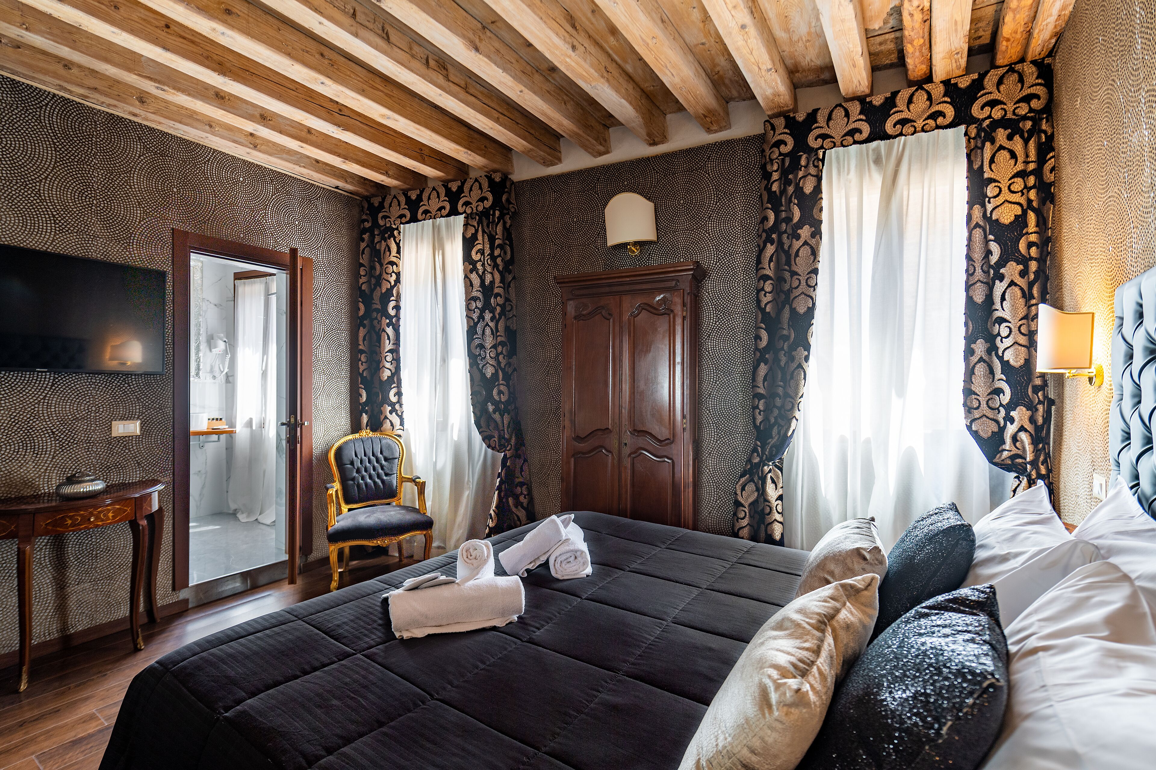 Quarto com uma cama grande, teto de madeira, televisão, escrivaninha e uma cadeira.