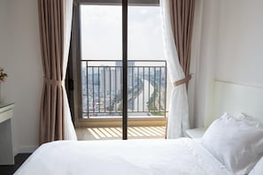 A hotel room with a bed, a desk, and a view of a cityscape through a balcony. - Rose Home (Ho Chi Minh City)
