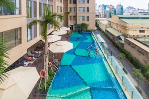 A rooftop swimming pool with multiple lanes, surrounded by lounge chairs and umbrellas, set against a cityscape backdrop. - Rose Home (Ho Chi Minh City)