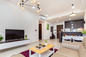 A modern living room with a flat-screen TV, a wooden coffee table, a sofa, and a dining area with a white table and chairs. - Rose Home (Ho Chi Minh City)