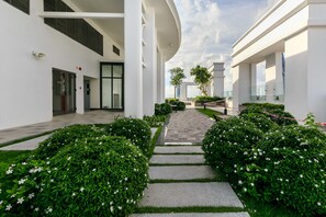 A modern building with a central pathway flanked by neatly trimmed bushes and white flowers. - Rose Home (Ho Chi Minh City)