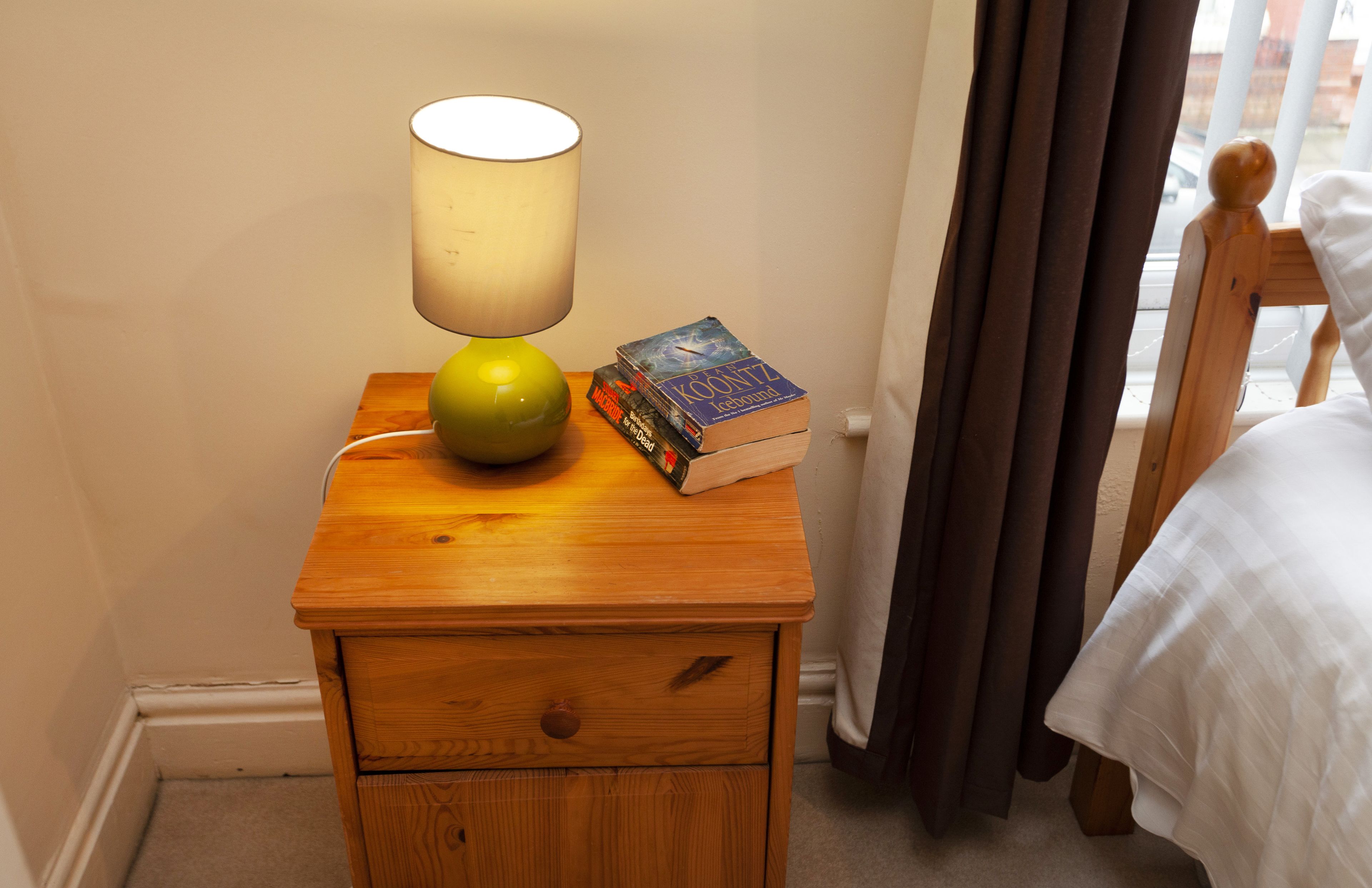 Una mesita de noche de madera con una lámpara, una manzana verde y una pila de libros.