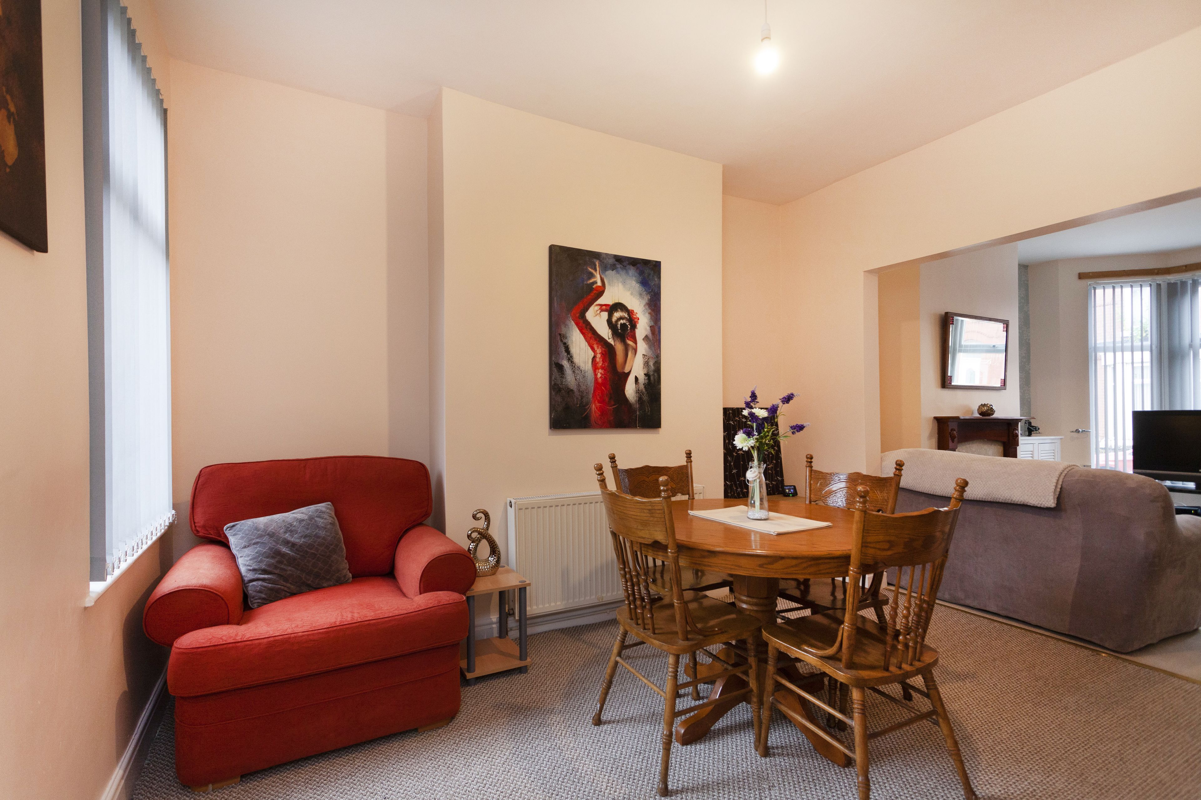 Una sala de estar con un sofá rojo, una mesa de comedor de madera y sillas, un cuadro en la pared y un televisor al fondo.