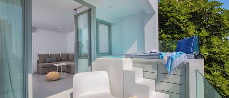 A modern outdoor living area with a white sofa, a round ottoman, and a small table with a book and a glass.