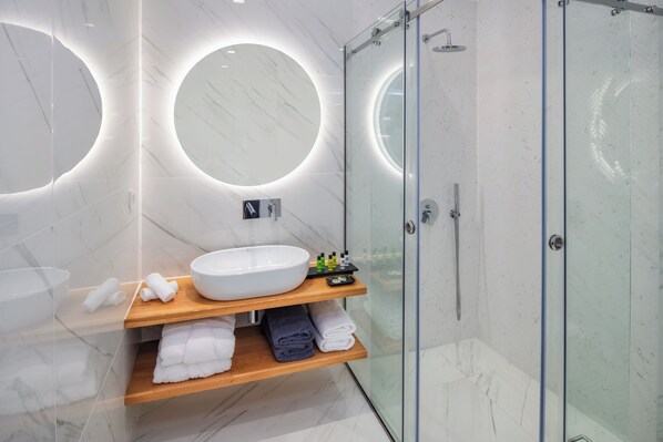 Un baño moderno con un espejo redondo grande, un lavabo blanco y una ducha con cerramiento de vidrio.