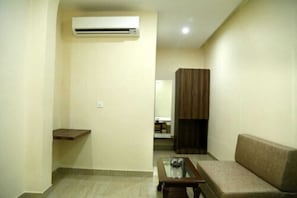 A living room with a sofa, a glass-top coffee table, a wooden shelf, a brown cabinet, and an air conditioning unit.