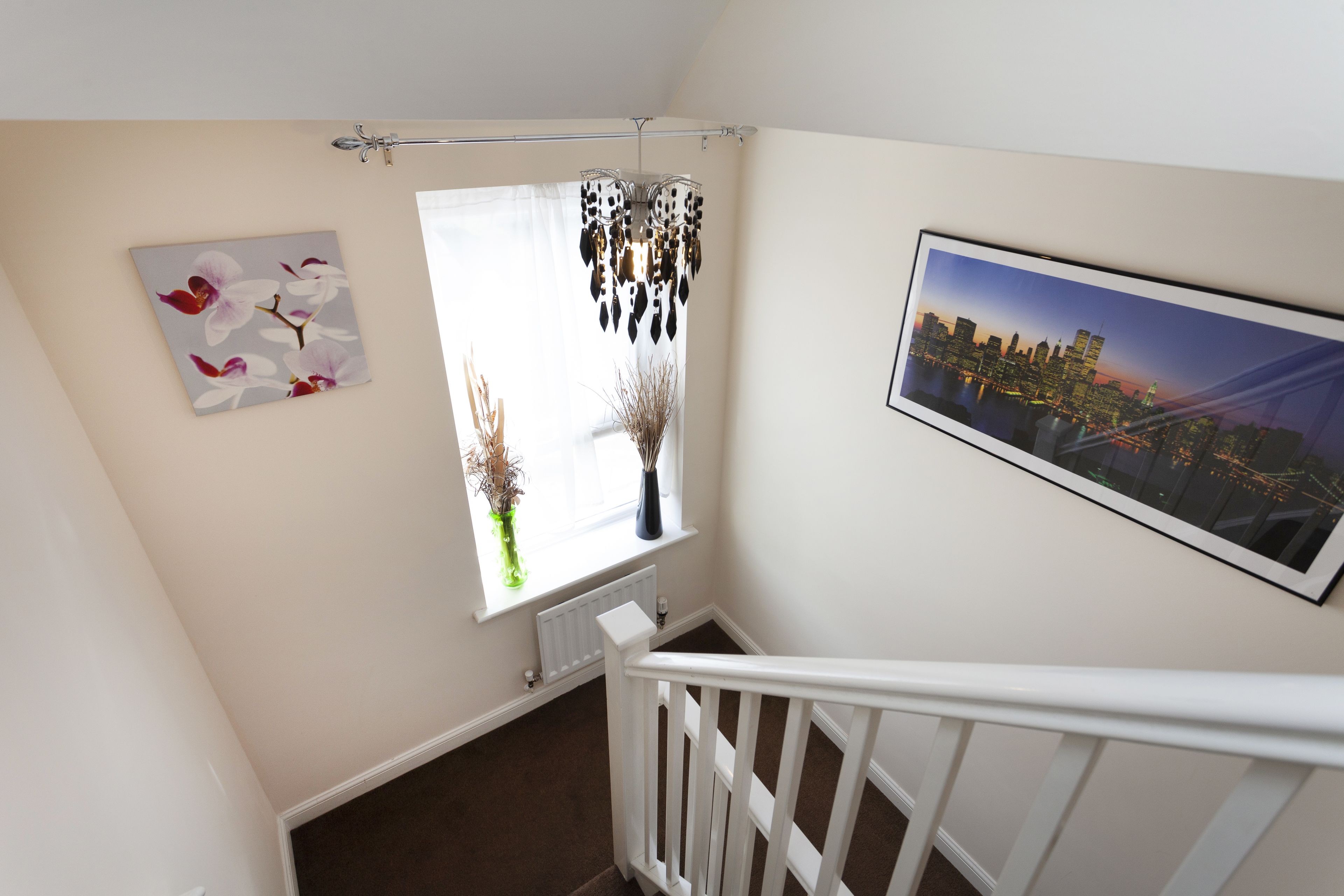 A staircase with a white railing, a cityscape view, a vase with dried plants, and a floral painting.